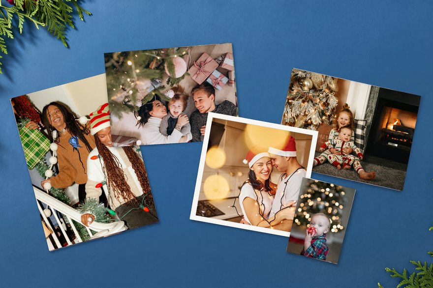 Holiday photo prints in different sizes, including a small wallet print, scattered on a blue background with evergreen branches, showing family and friends celebrating Christmas